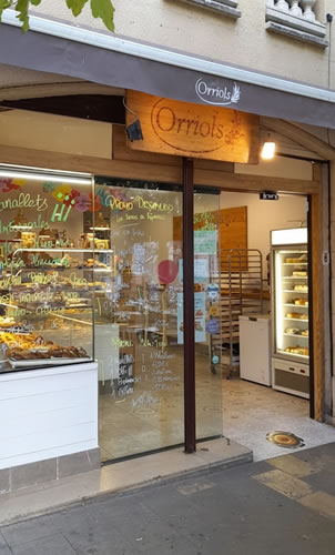 Escaparate y puerta de la panadería Orriols decorados con palabras de colores que destacan panes y dulces.